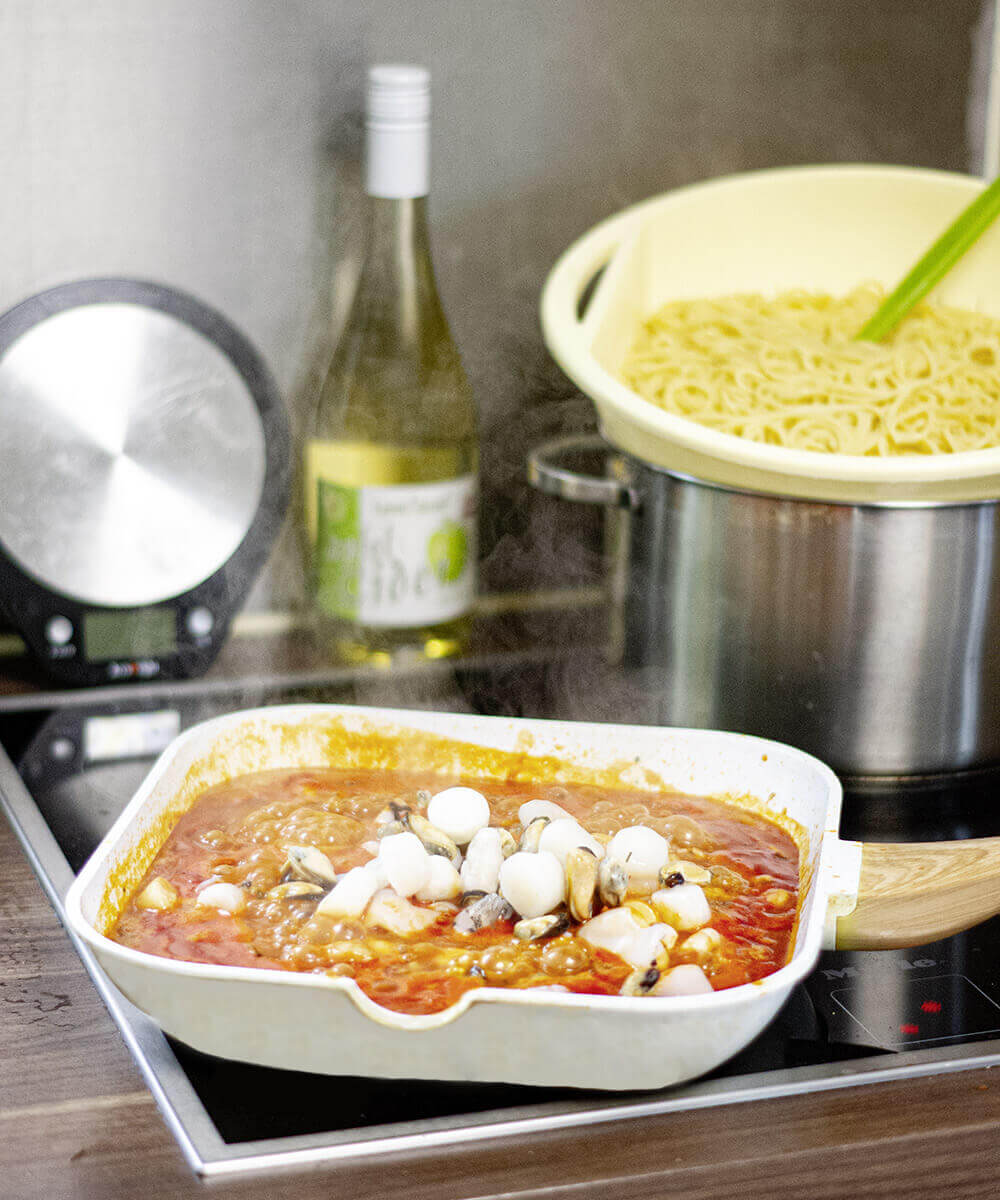 Spaghetti mit Meeresfrüchten und Cider steht am Herd